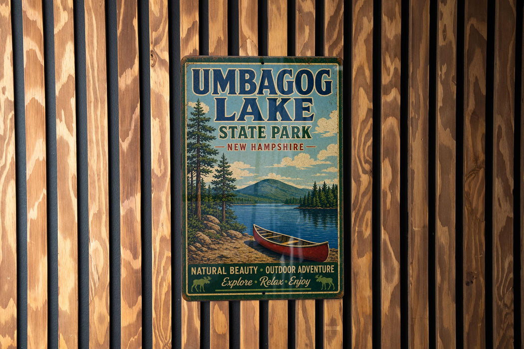A vintage-style metal sign for Umbagog Lake State Park in New Hampshire, featuring a scenic image of a lake, mountains, and a canoe.