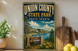 A vintage-style sign for Union County State Park in South Dakota, featuring a scenic landscape with a lake, mountains, and trees.