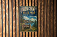 A vintage-style metal sign for Union County State Park in South Dakota, featuring a scenic landscape with a lake, mountains, and pine trees.