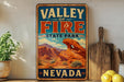 A vintage-style metal sign for Valley of Fire State Park in Nevada, featuring a desert landscape with mountains and a prominent rock formation.