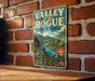 A vintage-style metal sign for "Valley of the Rogue State Park" is displayed on a brick wall, featuring a scenic mountain landscape.