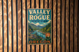 A vintage metal sign for "Valley of the Rogue State Park" is displayed on a wooden wall.