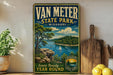 A vintage-style metal sign for Van Meter State Park in Missouri, featuring a scenic landscape with a lake, mountains, and a sailboat.