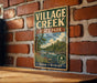 A vintage-style metal sign for "VILLAGE CREEK STATE PARK" in Texas, featuring a scenic landscape with a river and trees.