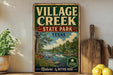 a vintage-style sign for " Village Creek State Park" in Texas, with a scenic illustration of a river, trees, and a cloudy sky. The sign is displayed on a wooden shelf, surrounded by various kitchen utensils and a potted plant.