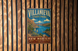 A vintage metal sign for Villanueva State Park in New Mexico, featuring a scenic landscape with mountains, a lake, and desert vegetation.
