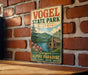 A vintage metal sign for Vogel State Park in Georgia, featuring a scenic illustration of a cabin surrounded by nature.