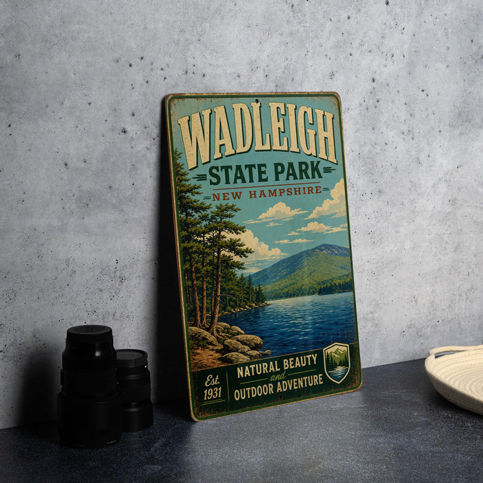 A vintage-style metal sign for Wadleigh State Park in New Hampshire, featuring a scenic landscape with a lake and mountains.