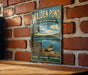 A vintage metal sign for Walden Pond, a state reserve in Massachusetts, featuring a scenic image of a lake with a boat and surrounded by trees.
