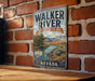 A vintage metal sign for the Walker River State Recreation Area in Nevada, featuring a scenic landscape with mountains, a river, and a forest.