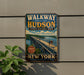 A vintage-style metal sign advertising the Hudson River Bridge in New York, featuring a scenic image of the bridge and people walking across it.