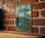 A vintage-style metal sign for Wallowa Lake State Park in Oregon, featuring a scenic mountain landscape with a lake and colorful wildflowers.