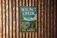 A vintage metal sign for Walnut Creek State Park in Oklahoma, featuring a scenic landscape with a lake and mountains.