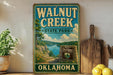 A vintage-style sign for Walnut Creek State Park in Oklahoma, featuring a scenic landscape with a lake and mountains.