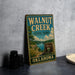 A vintage-style sign for Walnut Creek State Park in Oklahoma, featuring a scenic landscape with a lake and mountains.