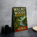 A vintage-style metal sign for Walnut Woods State Park in Iowa, featuring a scenic illustration of the park and its surroundings.