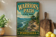 A vintage-style sign for Warrior's Path State Park in Pennsylvania, featuring a scenic mountain landscape with a winding trail.