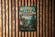 A vintage metal sign for Warrior's Path State Park in Tennessee, featuring a scenic illustration of a mountain landscape with a river and a Native American feather headdress.