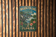 A vintage-style metal sign for Washington Oaks Gardens State Park in Florida, featuring a tropical landscape with palm trees, flowers, and a body of water.