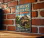 A vintage-style metal sign for Watkins Woolen Mill in Missouri, featuring an illustration of the mill and a waterfall.
