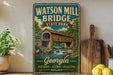 A vintage-style metal sign for Watson Mill Bridge State Park in Georgia, featuring an illustration of a covered bridge over a stream.
