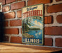 A vintage metal sign for the Wayne Fitzgerald Recreation Area in Illinois, featuring a scenic landscape with a lake and trees.