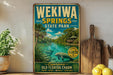 A vintage-style metal sign for Wekia Springs State Park, featuring a scenic image of the springs surrounded by lush greenery and a manatee.