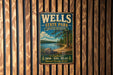 A vintage metal sign for Wells State Park in Massachusetts, featuring a scenic landscape with a lake, mountains, and trees.