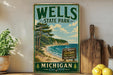 A vintage-style sign for Wells State Park in Michigan, featuring a scenic landscape with pine trees, a beach, and a lake.