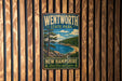 A vintage metal sign for Wentworth State Park in New Hampshire, featuring a scenic landscape with a lake, mountains, and pine trees.