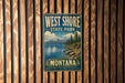 A vintage metal sign for West Shore State Park in Montana, featuring a scenic landscape with mountains, water, and pine trees.