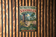 A vintage metal sign for Weymouth Woods Sandhills Nature Preserve, featuring a scenic landscape with a pine tree, flowers, and a dirt path.