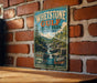 A vintage-style metal sign for Whestone Gulf State Park, featuring a scenic image of a waterfall and forest, mounted on a brick wall.