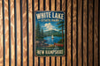 A vintage metal sign for White Lake State Park in New Hampshire, featuring a scenic landscape with a lake, mountains, and a sailboat.