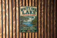 A vintage-style metal sign for White Oak Lake State Park in Arkansas, featuring a scenic image of the lake and surrounding landscape.