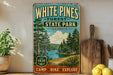 A vintage-style sign for White Pines Forest State Park in Illinois, featuring a scenic illustration of pine trees, a lake, and mountains.