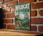 A vintage metal sign for Wildcat Mountain State Park in Wisconsin, featuring a scenic landscape with a mountain, trees, and a river.