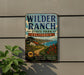 A vintage metal sign for Wilder Ranch State Park in California, featuring a scenic landscape with a house, trees, and a winding path.