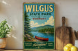 A vintage-style metal sign for Wilgus State Park in Vermont, featuring a scenic image of a red canoe on a lake surrounded by pine trees and mountains.