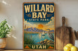 A vintage-style metal sign for Willard Bay State Park in Utah, featuring a scenic landscape with mountains, a lake, and a crane.