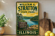 A vintage-style sign for William G. Stratton State Park in Illinois, featuring a scenic landscape with a river and mountains.