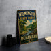 A vintage metal sign for Wilmington State Parks in Delaware, featuring a scenic landscape with a river and bridge.