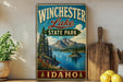 A vintage-style sign for Winchester Lake State Park in Idaho, featuring a scenic landscape with mountains, pine trees, and a lake.