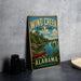 A vintage-style metal sign for Wind Creek State Park in Alabama, featuring a scenic image of a lake with a canoe and surrounded by pine trees.
