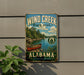 A vintage-style metal sign for Wind Creek State Park in Alabama, featuring a scenic image of a canoe on a lake surrounded by pine trees.