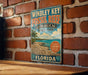 A vintage-style metal sign for Windley Key Fossil Reef, a geological state park in Florida, is displayed on a brick wall.