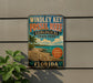 A vintage-style metal sign for Windley Key, Fossil Reef, and Florida State Park, featuring a tropical beach scene with palm trees and a fossil.