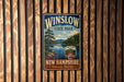 A vintage metal sign for Winslow State Park in New Hampshire, featuring a scenic landscape with a lake and pine trees.
