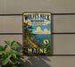 A vintage-style metal sign for Wolf's Neck Woods State Park in Maine, featuring a scenic landscape with a path, trees, and a body of water.