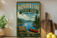 A vintage-style sign for Wonder Lake State Park in New York, featuring a scenic image of a lake surrounded by pine trees and mountains.
